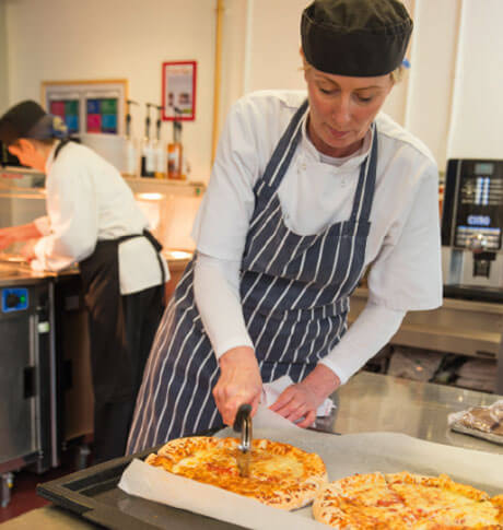 Cafeteria member cutting pizza in the kitchen